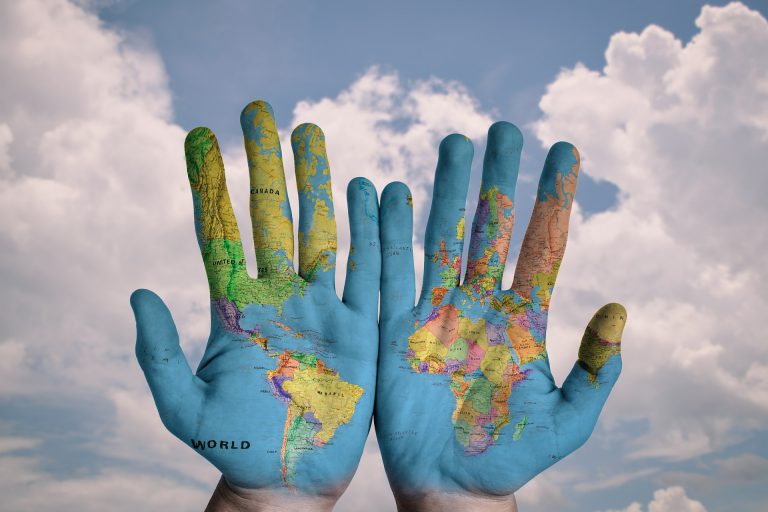 IMG_20170121_235715996 Two hands raised against a cloudy sky, painted with a world map showing continents and countries.