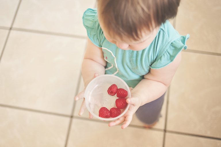 pexels-photo-302482 Child holding a small bowl with several raspberries, standing on a tiled floor.