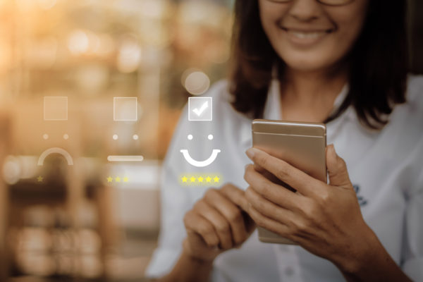 Person smiling and holding a smartphone. A floating interface displays a satisfaction survey with a happy face selected and checked, highlighting the success of qualitative research in capturing genuine feedback.