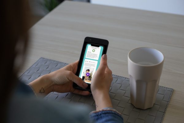 Person holding a smartphone over a table with a gray placemat and a white ceramic cup, reading an app with green accents.