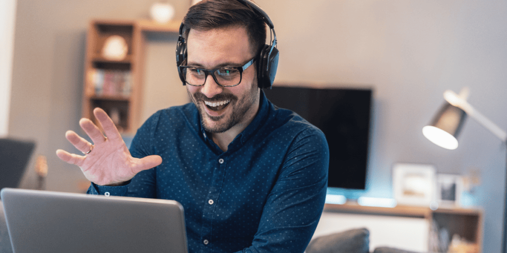 man waving at computer screen while wearing headphones