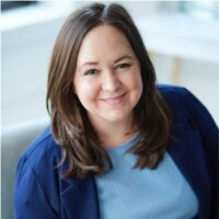 Sarah Tomasaiti with long brown hair wearing a blue shirt and dark blazer, smiling at the camera.