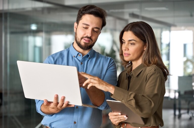 Two busy professional business people working in office with computer. Middle aged female executive manager talking to male colleague having conversation showing software online solution on laptop.