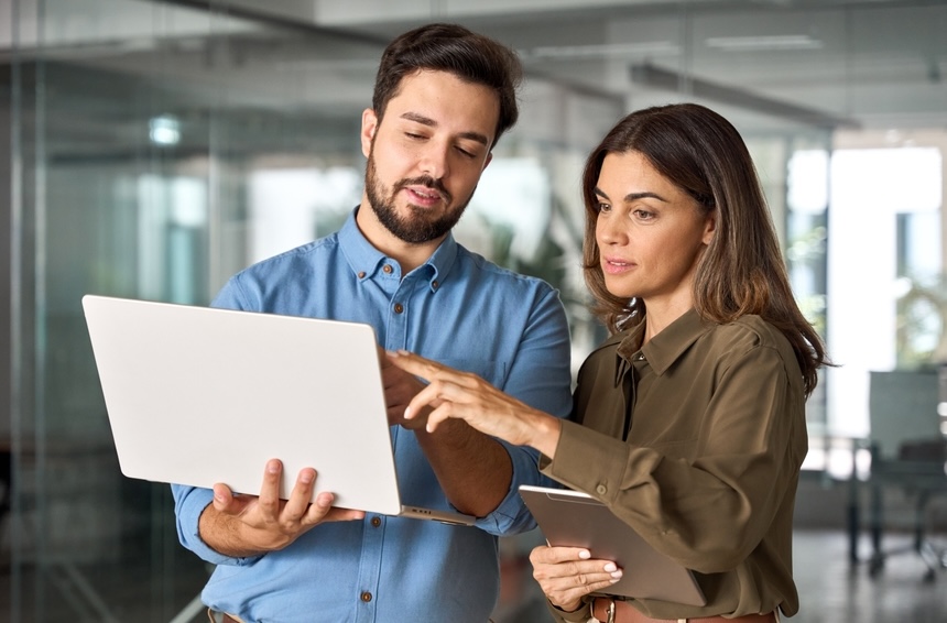 Two,Busy,Professional,Business,People,Working,In,Office,With,Computer. Two busy professional business people working in office with computer. Middle aged female executive manager talking to male colleague having conversation showing software online solution on laptop.