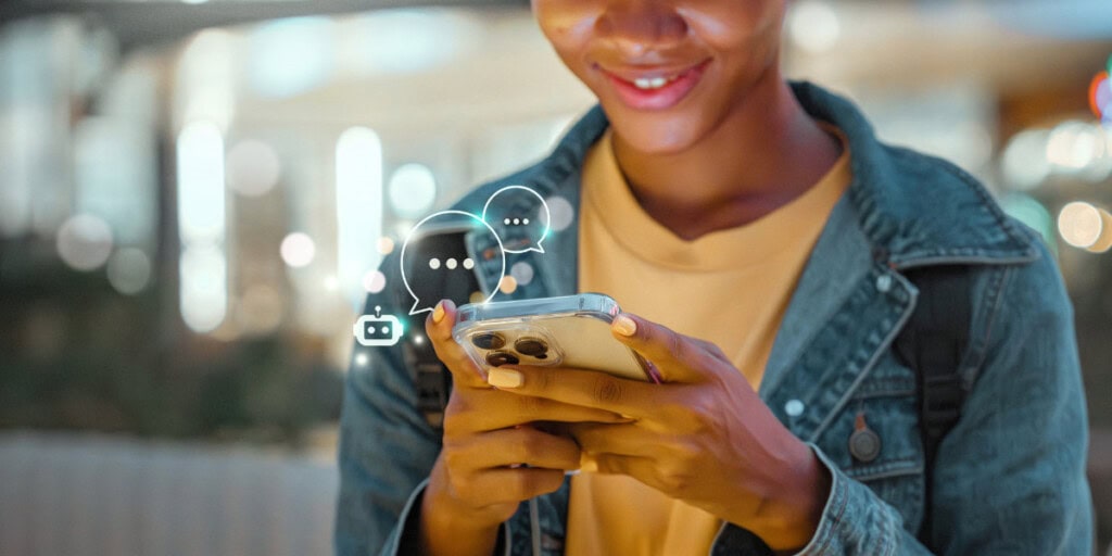 A person holding a smartphone, smiling while typing, with chat and bot icons digitally superimposed near the screen.